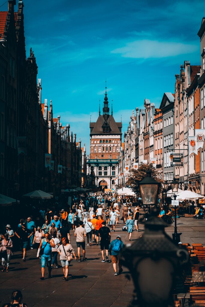 Kolorowe zdjęcie. Miasto Gdańsk. Tłum zwiedzających na Starym Mieście. Niebieskie niebo. Ludzie kolorowo ubrani.